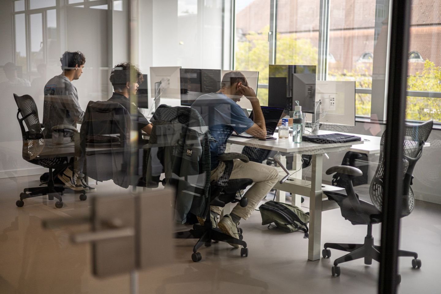 Drie developers in een glazen ruimte aan het werk achter de laptop.